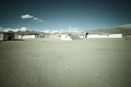 Few old houses, rocky mountains and scorched valley on a background of blue sky with a few white clouds.  Tonedの写真素材