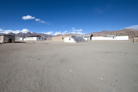 Few old houses, rocky mountains and scorched valley on a background of blue sky with a few white clouds.の写真素材