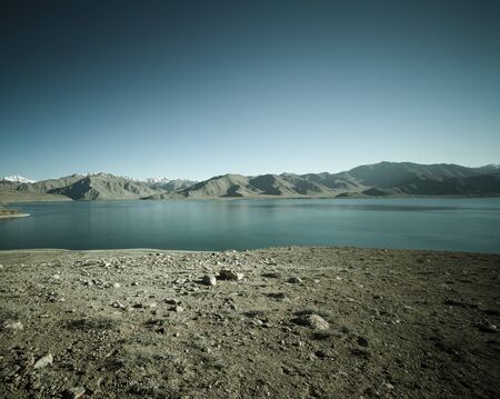 Beautiful landscape - clear mountain lake in rocky valley. The rocky mountains and blue sky are behind. Toned.の写真素材