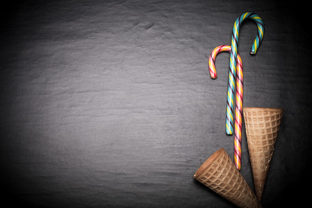 Candy sticks and waffle cones for ice cream on a black background. Space for text. Toned.の写真素材