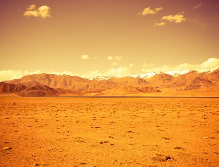 Rocky mountains and scorched valley on a background of blue sky with a few white clouds. Toned.の写真素材