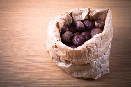 Chestnuts in a paper bag on a light wooden table. Toned.の写真素材