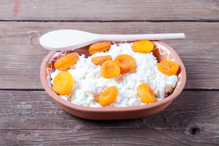 Fresh cottage cheese with dried apricots in pottery on old wooden table.の写真素材