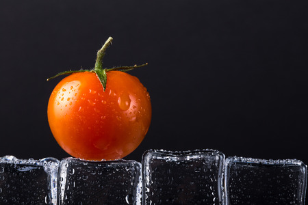 Fresh tomato on wet ice cubes on black background. Selective focus.の写真素材