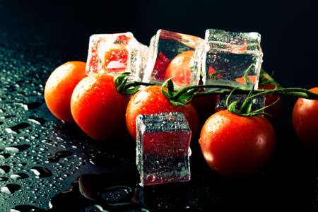 Banch of red cherry tomatos and ice cubes on black wet table. Selective focus. Toned.の写真素材
