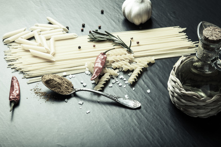 Different kinds of pasta, red chili pepper, rosemary, sea salt and spices on a black background. Selective focus. Toned.の写真素材
