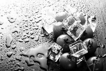 Banch of red cherry tomatos and ice cubes on black wet table. Selective focus. Toned.の写真素材
