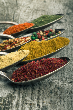 Antic metal spoons with different kinds of spices on old wooden board. Selective focus. Toned.の写真素材