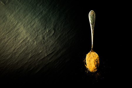 Old metal spoon with spices on a black background. Toned.の写真素材