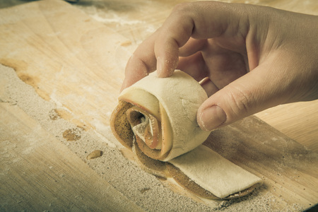Female hand twists the apple slices in the dough strip on a light wooden table with flour. Toned.の写真素材