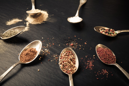 Spices in old metal spoons on black background. Toned.の写真素材
