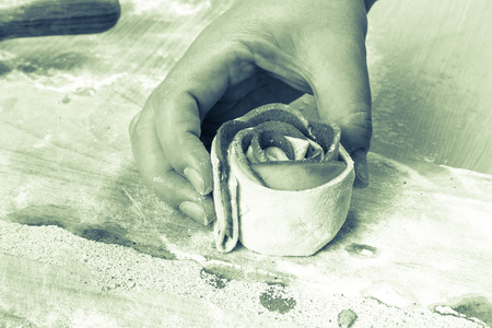 Female hand twists the apple slices in the dough strip on a light wooden table with flour. Toned.の写真素材
