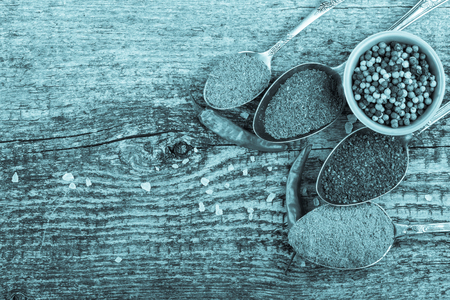 Antic metal spoons and small bowl with different kinds of spices on old wooden board. Selective focus. Toned.の写真素材