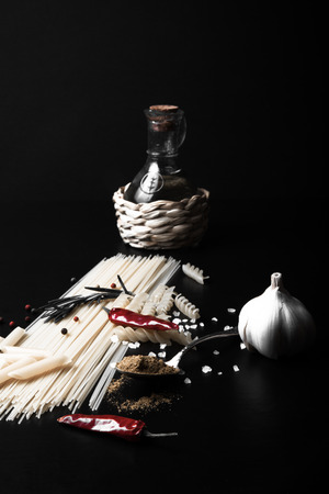 Different kinds of pasta, red chili pepper, rosemary, sea salt and spices on a black background. Selective focus. Toned.の写真素材