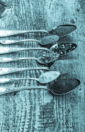 Antic metal spoons with different kinds of spices on old wooden board. Selective focus. Toned.の写真素材