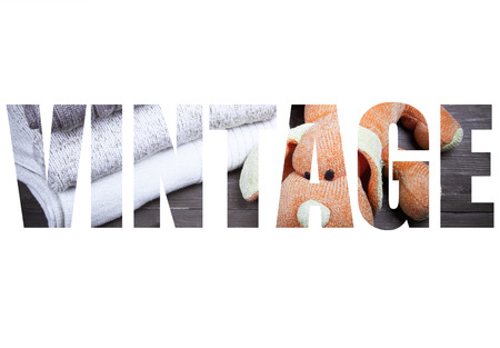 Word VINTAGE over knitted toy dog and stack of knitting clothes on wooden table opposite a stony...