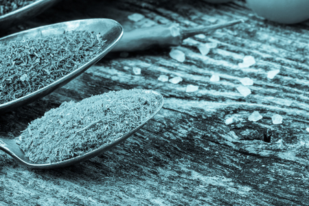 Antic metal spoons with different kinds of spices on old wooden board. Selective focus. Toned.の写真素材