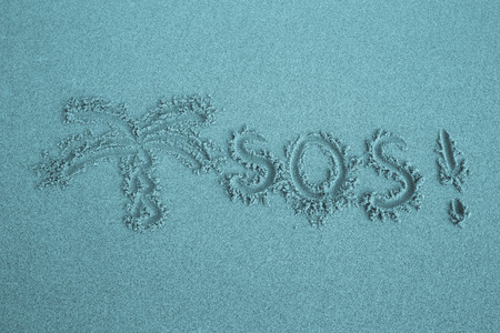 The inscription on the sand beach "SOS" and a symbolic image of palm trees.の写真素材