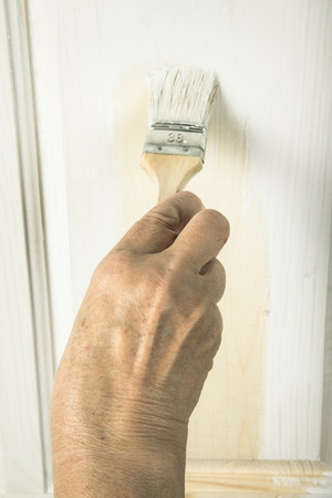 Hand of an elderly woman with a paint brush with white paint door. Selected focusの写真素材