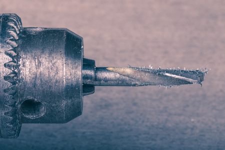 Drill with a drill bit and metal shavings on a blurred background of the board of the old wooden table. Closeup. Toned.の写真素材