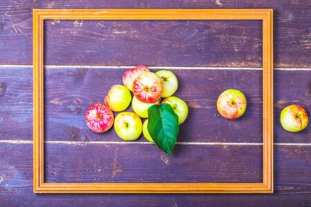 Red-yellow seasonal apples with leaf in wooden frame on the background of old boards. Toned.
