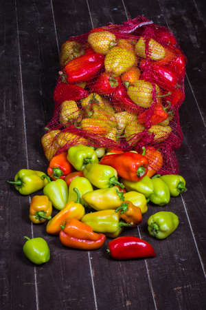 Mesh bag with colorful sweet peppers on the old wooden floor. Selective focus. Toned.の写真素材