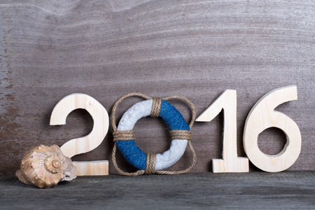 Lifebuoy instead of the digit 0 in the number 2016 and seashell on gray wooden background.