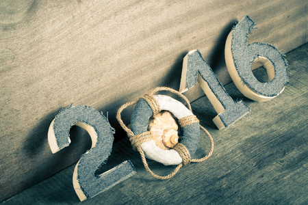 Lifebuoy instead of the digit 0 in the number 2016 and seashell on gray wooden background. Toned.