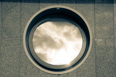 Ajar round window on the tiled granite wall - part of the urban architecture. Toned.