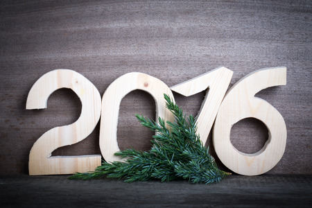Wooden figures 2016 and branch of the Christmas tree on gray wooden background. Toned.