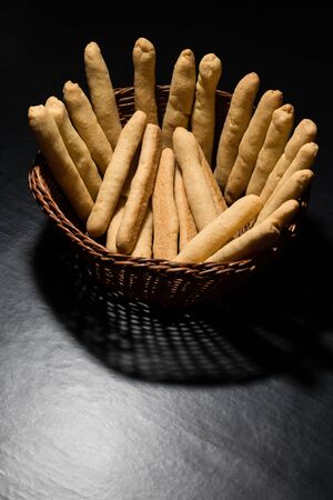 Fresh baked cheese sticks in a wicker wooden basket on black tableの写真素材