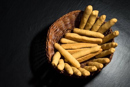Fresh baked cheese sticks in a wicker wooden basket on black table