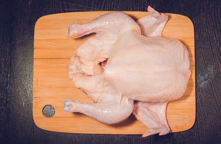 Fresh whole chicken is prepared for cooking on a light wooden cutting board on a black table. Toned.の写真素材