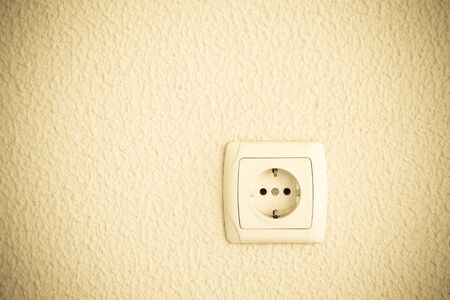 Light plastered wall with electric outlet for background.