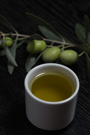 Branch of olive tree with green olive berries and cap of fresh olive oil on a black wooden table or board.の写真素材