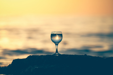 Glass of white vine with reflections of sun and sea on the background of beautiful sunset. Selective focus. Toned.の写真素材