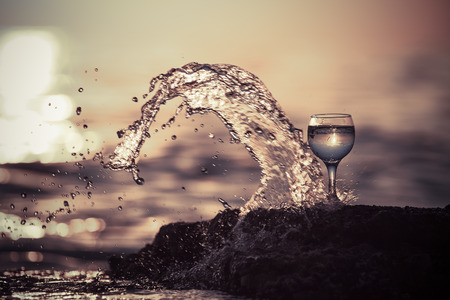 Glass of white vine with reflections of sun and sea on the background of beautiful sunset. Selective focus. Toned.の写真素材