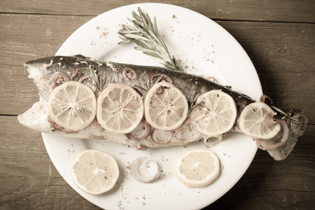 Fish Nelma with lemon, onion and rosemary on a wooden table. Toned.の写真素材