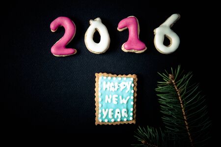 Gingerbread homemade cookies with icing and christmas tree branch on a black table or board for...