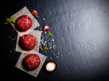 Raw ground beef meat steak cutlets with herbs and spices on black table or board for background. Selective focus. Toned.の写真素材
