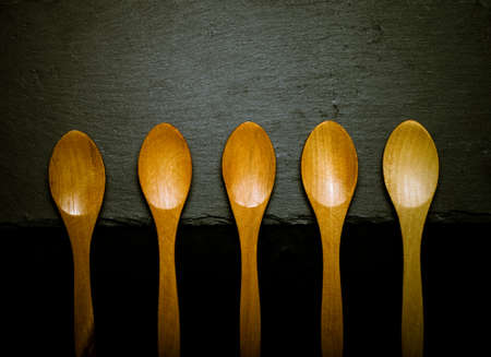 Wooden spoons on a plate of slate on a black background. Toned.