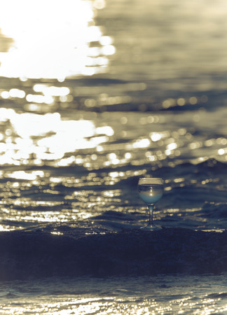 Glass of white vine with reflections of sun and sea on the background of beautiful sunset. Selective focus. Toned.の写真素材