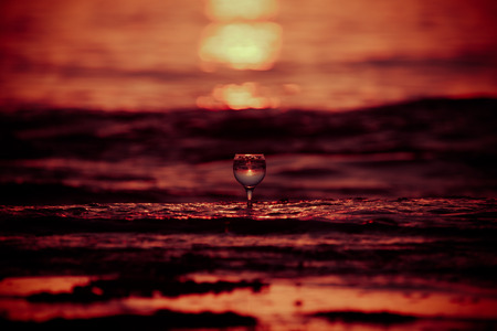Glass of white vine with reflections of sun and sea on the background of beautiful sunset. Selective...