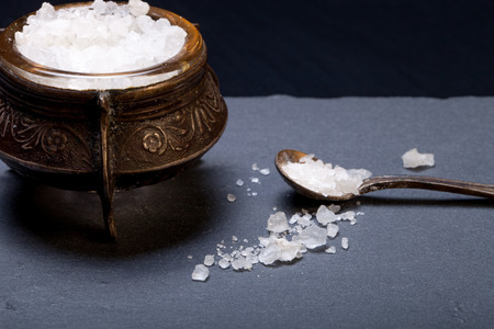 Sea salt in an old salt shaker on a plate of slate on a black background.の写真素材