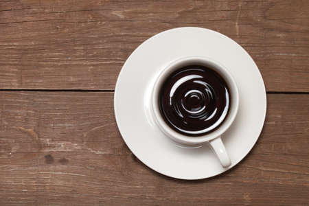 White cup of coffee on old wooden table.