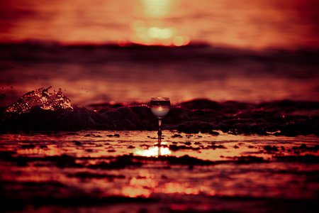 Glass of white vine with reflections of sun and sea on the background of beautiful sunset. Selective focus. Toned.の写真素材
