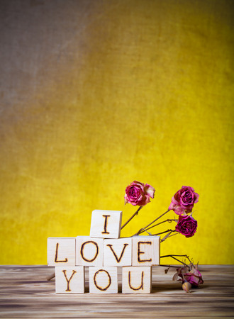 Wooden cubes and dry rose flowers on new wooden board and burlap background. Toned.の写真素材