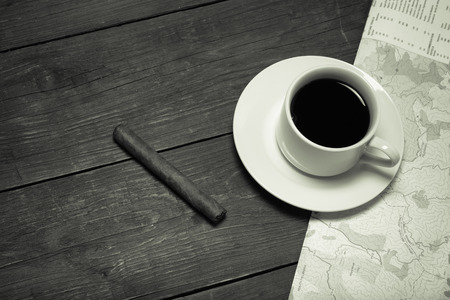 White cup of coffee, map and cigar on old wooden table. Toned.の写真素材