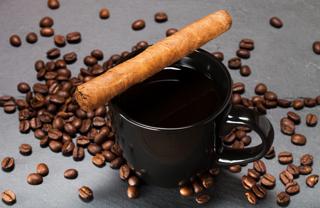 Black cup of coffee, cigar and coffee seeds on the slate background.の写真素材
