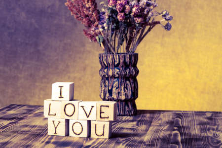 Wooden cubes with inscription "I LOVE YOU" and bouquet of dry flowers on new wooden board and burlap background. Selective focus. Toned.の写真素材